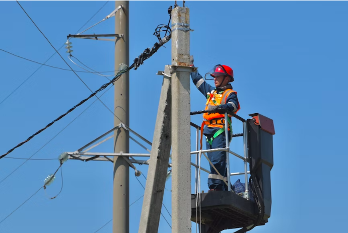 A person checking wires and other electrical elements on a poll.